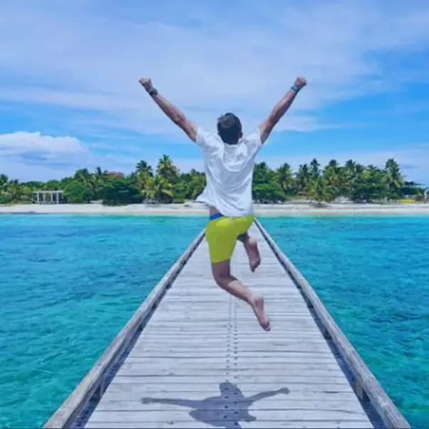 Person jumping with joy on a tropical beach pier